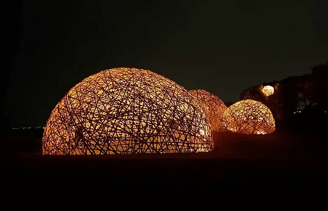 Photo de nuit de plusieurs dômes en bambou éclairés de l'intérieur.